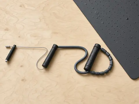 Two jump ropes, a thin speed cable and a thicker rope, on a light floor next to a black rubber mat